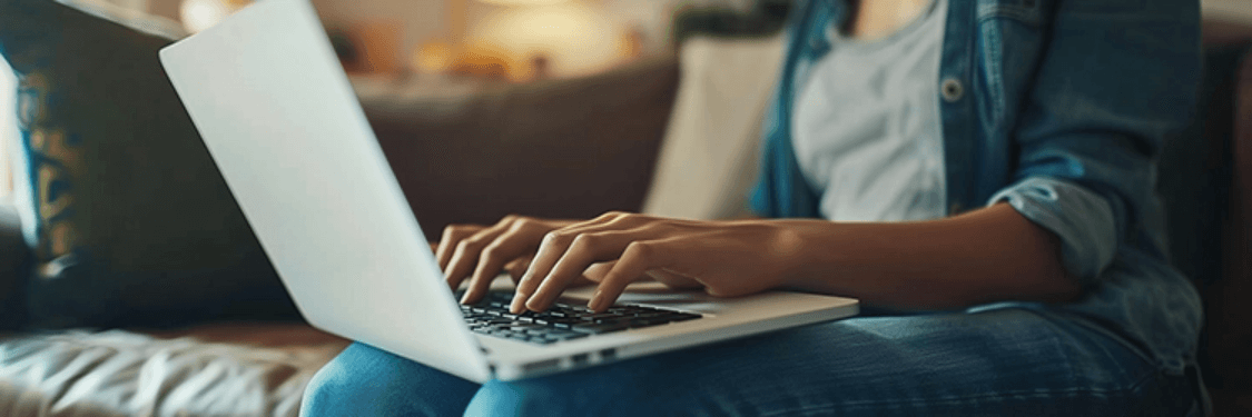 Close-up of woman's hands typing on laptop in a living room