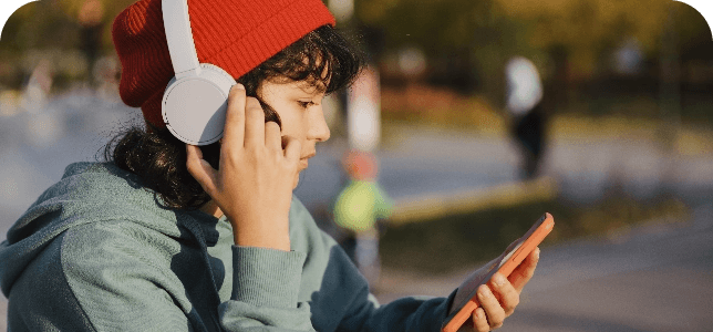 Young person wearing headphones and a beanie looking at mobile phone