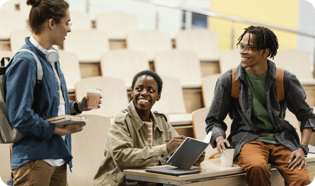 Three college students sitting in a lecture hall talking to one another